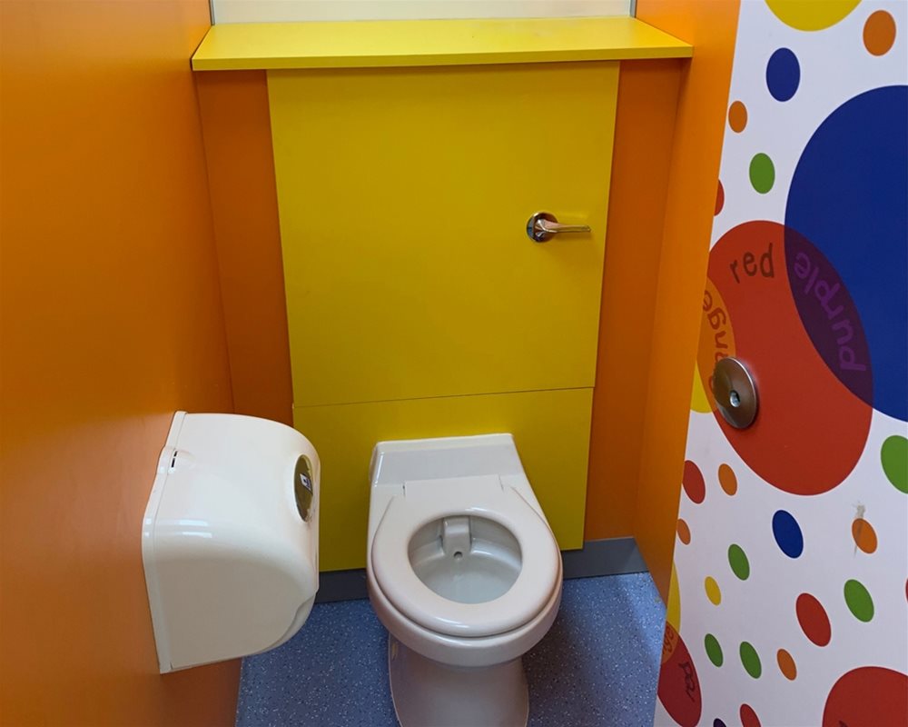 Colourful toilet cubicle with coloured spots on the door and a low down toilet for children