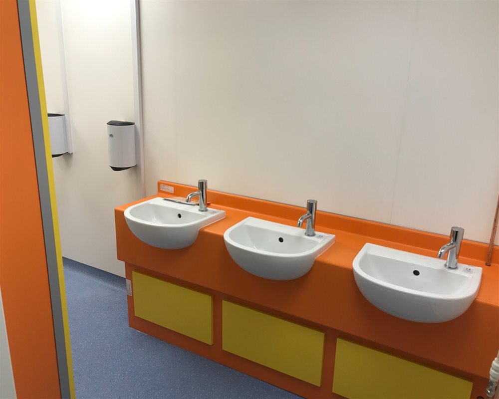 Three small vanity basins with orange and yellow surrounds in a childrens washroom 