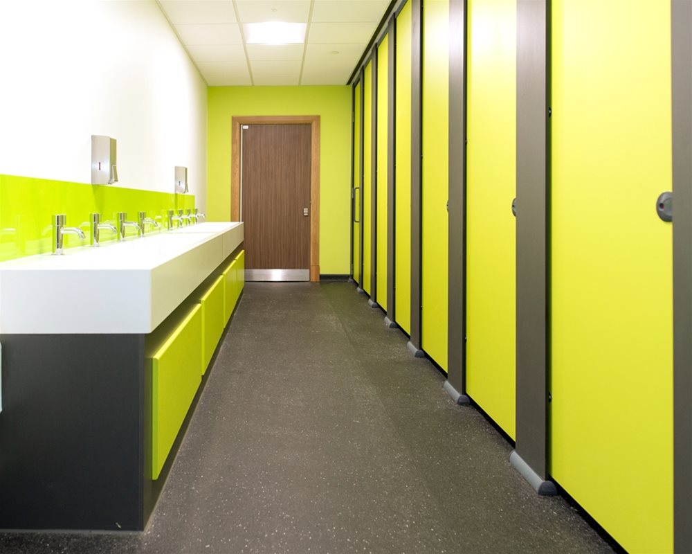 Multiple green toilet cubicles with vanity units opposite