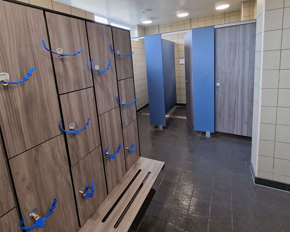 Swimming pool changing room with 'Baseline' shower cubicles in 'Grey Oak' and lockers and benching with wristband keys.