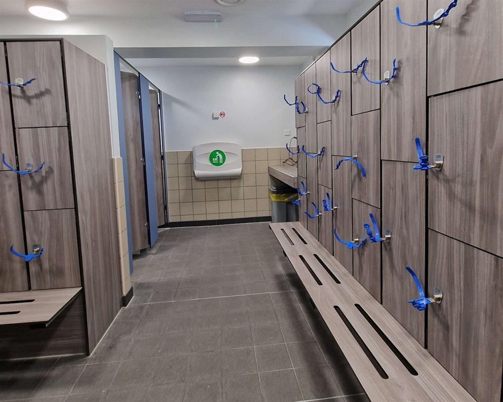 Swimming pool changing room with 'Baseline' toilet cubicles in 'Grey Oak' and lockers with wristband keys and integrated benching .