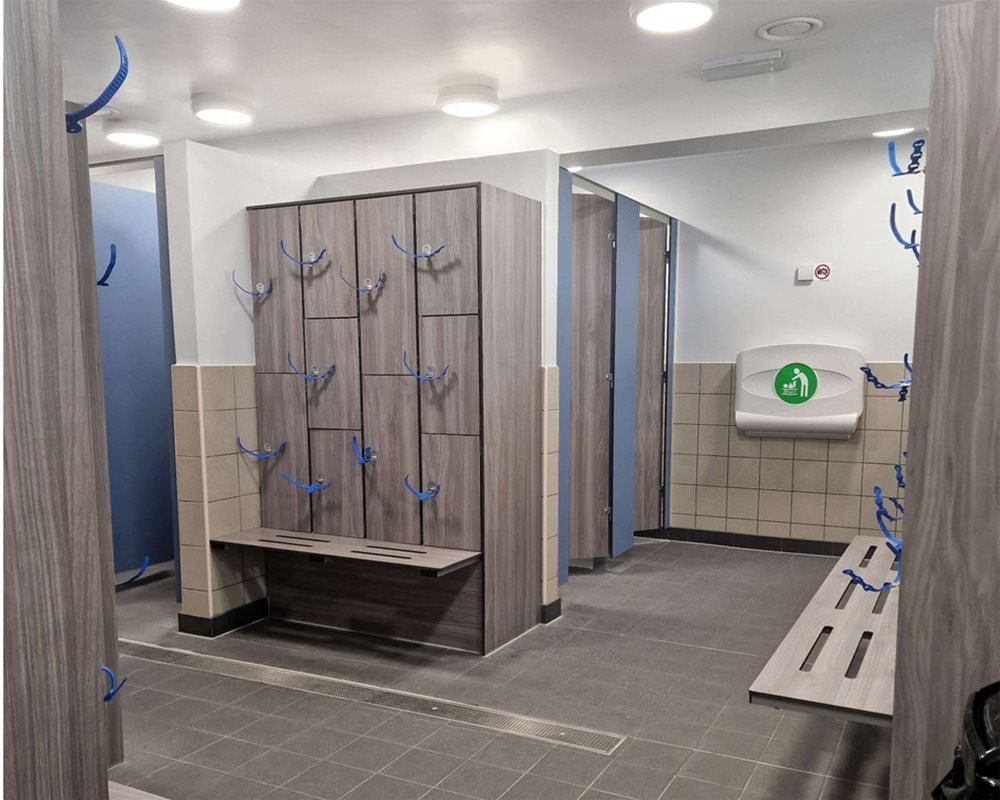 Swimming pool changing room with 'Baseline' toilet cubicles in 'Grey Oak' and lockers with wristband keys and integrated benching.