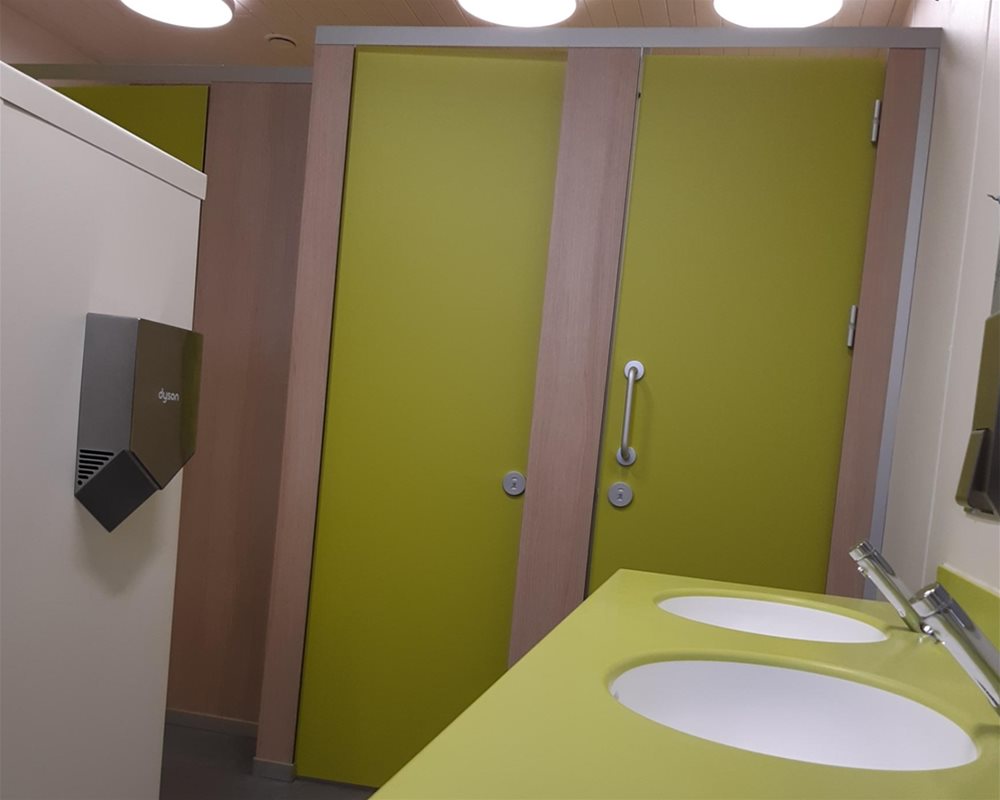 'Apple' solid surface counter top vanity unit with sensor taps and 'Lime Green' and 'Bleached Oak' HiZone for Schools full height toilet cubicle.