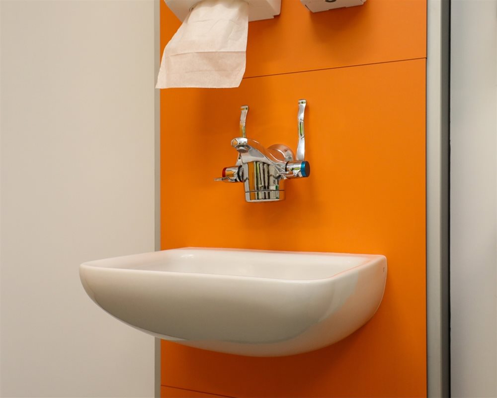 Close up of healthcare IPS boxed out unit in 'Orange' with clinical wash basin and wall mounted lever healthcare taps in hospital room.