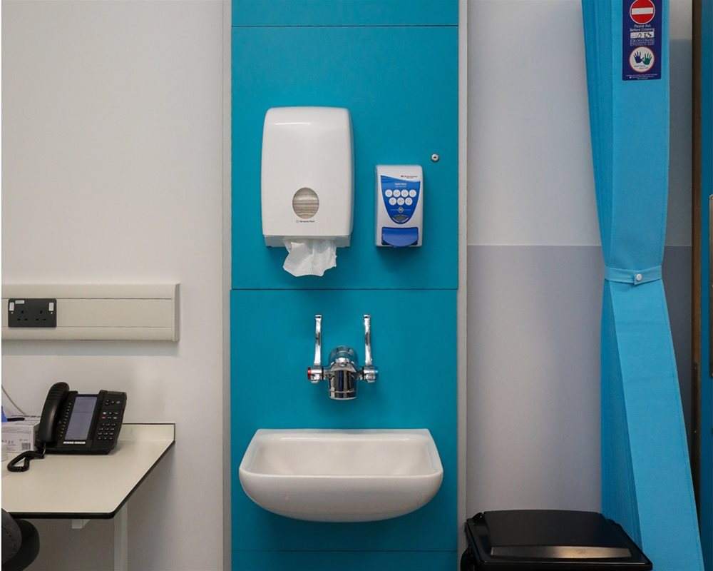 Healthcare IPS boxed out unit in 'Turquoise' with clinical wash basin and wall mounted lever healthcare taps, tissue dispenser and soap dispenser in hospital room.