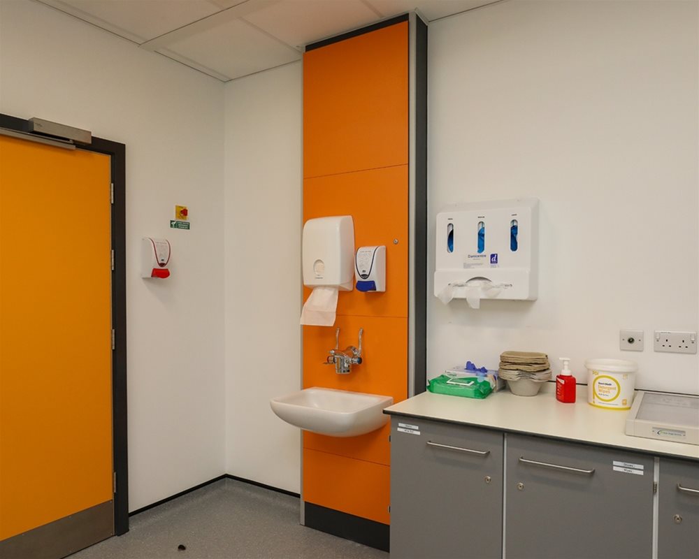 Healthcare IPS boxed out unit in 'Orange' with clinical wash basin and wall mounted lever healthcare taps in hospital room.