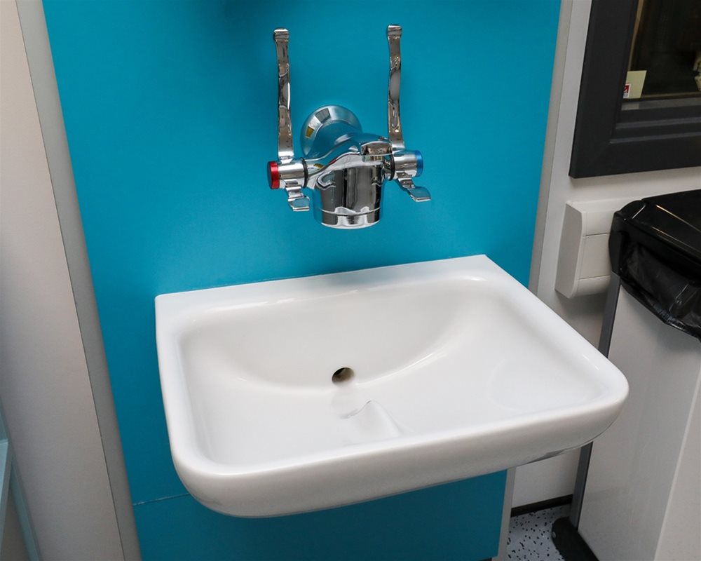 Close up of healthcare IPS boxed out unit in 'Turquoise' with clinical wash basin and wall mounted lever healthcare taps in hospital room.