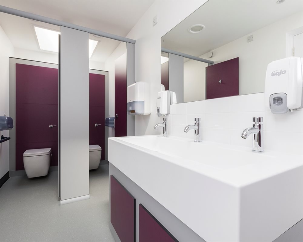Washroom with open toilet cubicles and Marden wall hung white toilets on 'Mulberry' purple panel